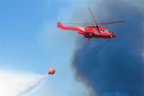 Helikopter gaśniczy zrzucający wodę na pożar w górskim, zalesionym terenie