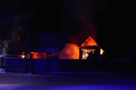Tematyczne zdjęcie płonącego budynku gospodarczego nocą, z widocznymi strażakami