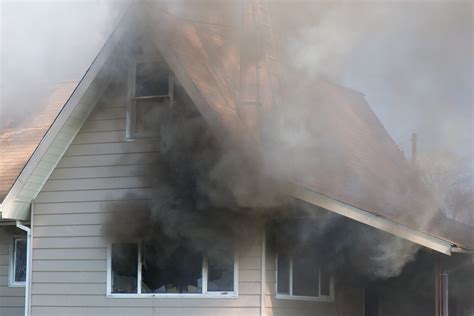 Photo of a residential house severely damaged by fire, with visible smoke or charring.
