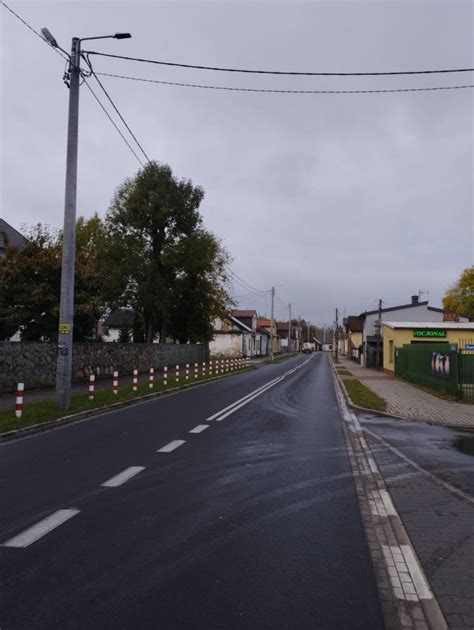 Zdjęcie nowego, lśniącego hydrantu ulicznego w miejscowości wiejskiej, z wyraźnie widocznym otoczeniem.