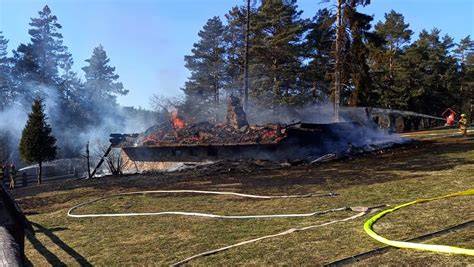 Fotografia płonącego drewnianego ośrodka wypoczynkowego otoczonego przez strażaków