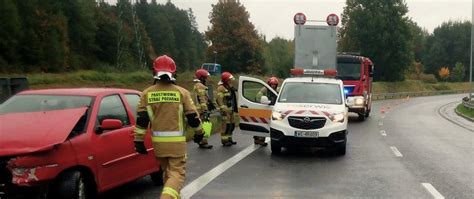 zdjęcie płonącego samochodu osobowego na poboczu drogi, z widocznymi strażakami gaszącymi ogień