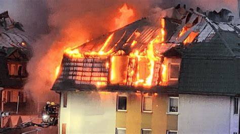 Fotografia strażaków gaszących pożar w budynku jednorodzinnym, z widocznym dymem