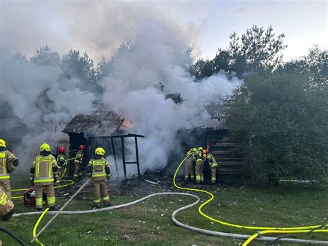 zdjęcie z akcji gaśniczej przedstawiające płonący drewniany dom z dachem krytym strzechą
