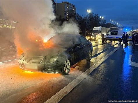 Policjanci i cywile gaszący płonący samochód na drodze