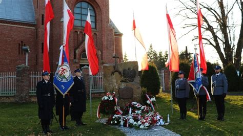 Znicze i hełmy strażackie złożone w hołdzie na tle pomnika upamiętniającego poległych strażaków