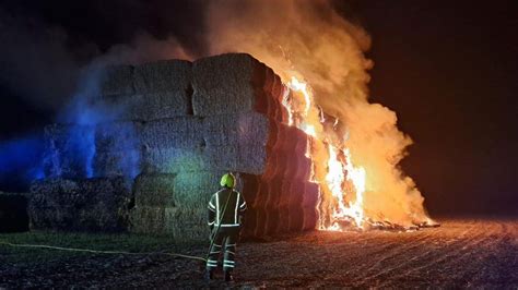 Photo of firefighters extinguishing a large hay bale fire in a rural setting, Komorowo, Brodnica district