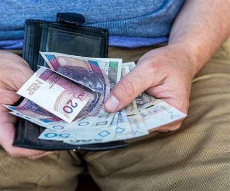 Ręce składające pieniądze do słoika lub cegły układane na fundamencie symbolizujące odbudowę