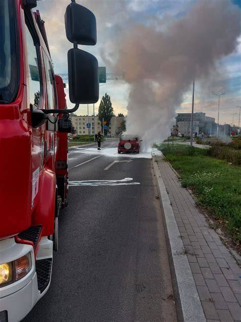 Zdjęcie przedstawiające strażaków gaszących płonący samochód osobowy blisko budynku mieszkalnego