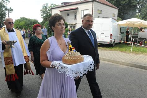 Zdjęcie z dożynek gminnych w Czarnocinie, przedstawiające Mariolę Dybała jako starostę dożynek, wręczającą chleb wójtowi, z widocznymi pocztami sztandarowymi OSP w tle.