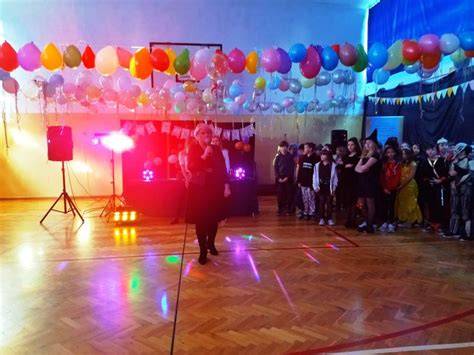 Zdjęcie z balu karnawałowego w hali sportowej, pokazujące dzieci w strojach i animatorów.