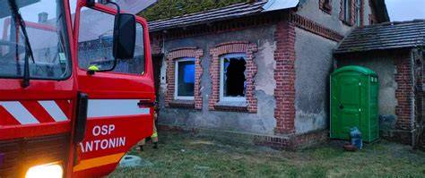 Wóz strażacki i strażacy gaszący pożar w budynku mieszkalnym