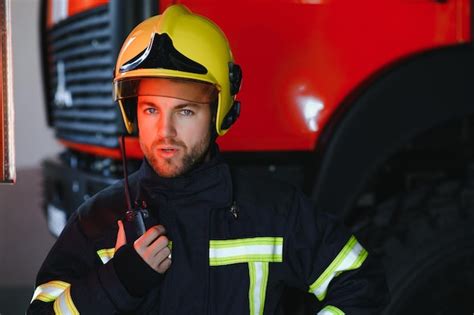 Portret księdza Dawida Gawendy w stroju strażaka na tle wozu strażackiego