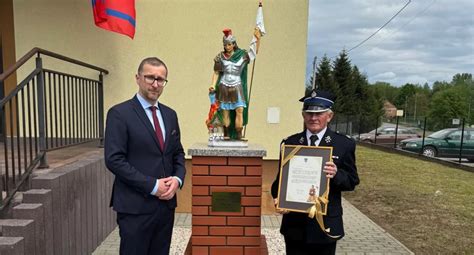 Zdjęcie przedstawiające współczesny sztandar OSP oraz figurę św. Floriana na frontonie budynku