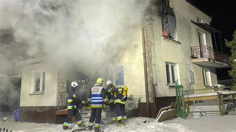 Zdjęcie przedstawiające miejsce pożaru domu, z widocznymi służbami ratunkowymi: straż pożarna, policja, prokurator.
