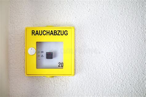 Thematic photo of a bright orange smoke exhaust button on a wall in a building corridor.