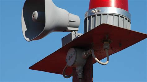 Ilustracja przedstawiająca ręczną syrenę alarmową z widoczną korbą.