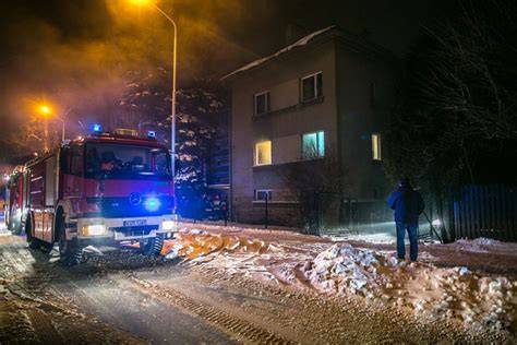 Zdjęcie przedstawiające akcję gaśniczą w płonącym budynku mieszkalnym nocą, z widocznymi płomieniami i strażakami