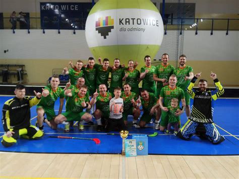 Zdjęcie przedstawiające uczniów grających w unihokeja w hali sportowej, z kibicami na trybunach