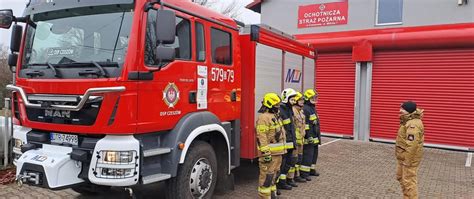 Ilustracja przedstawiająca grupę strażaków przy nowoczesnym wozie strażackim podczas festynu