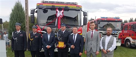 Grupa strażaków OSP podczas ceremonii, w tle wóz strażacki