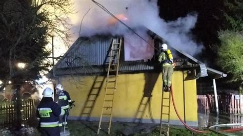 strażacy gaszący pożar drewnianego domu w dzień