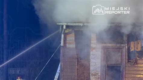 Strażacy gaszący pożar dachu domu jednorodzinnego, dym unoszący się z budynku