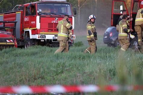 Widok na zadymione budynki gospodarcze objęte pożarem, z widocznymi strażakami w akcji