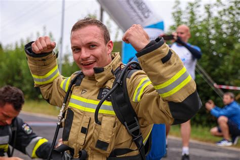 Uczestnicy zawodów narciarskich w pełnym stroju strażackim z hełmami, sfotografowani na tle zaśnieżonego stoku.