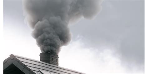 Zdjęcie przedstawiające dym o charakterystycznym, ciemnym kolorze unoszący się z komina lub z ogniska na posesji