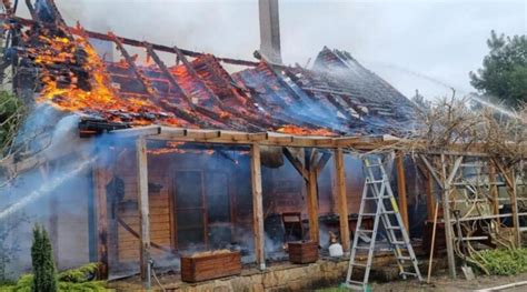 Zgliszcza spalonego drewnianego domu jednorodzinnego, otoczone taśmą policyjną, symbolizujące miejsce tragedii.