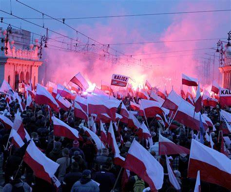 Tematyczne zdjęcie Marszu Niepodległości w Warszawie, z widocznym tłumem i elementami pirotechniki.