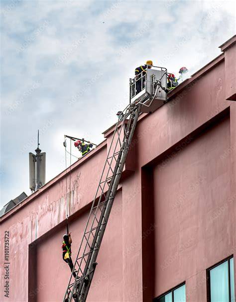 Firefighters using a ladder platform to extinguish flames on the roof of a building during the night.