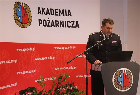 Zdjęcie przedstawiające budynek Akademii Pożarniczej oraz uroczystą zbiórkę funkcjonariuszy i studentów uczelni.