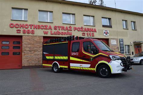 zdjęcie wozów strażackich OSP Luboń z zapalonymi światłami w tle remizy