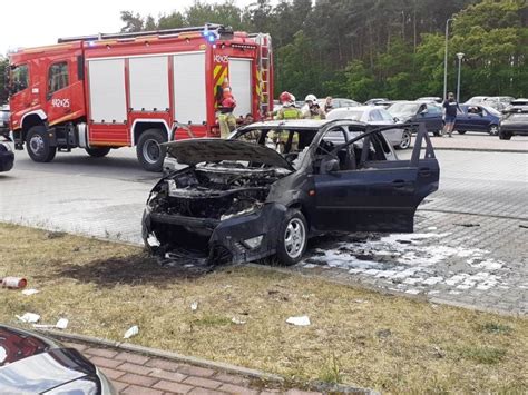 Zdjęcie spalonego samochodu osobowego na parkingu, otoczonego przez strażaków