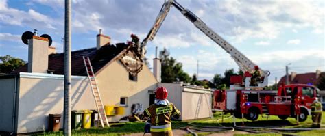 Strażacy gaszący pożar poddasza budynku mieszkalnego, używający prądów wody z drabin