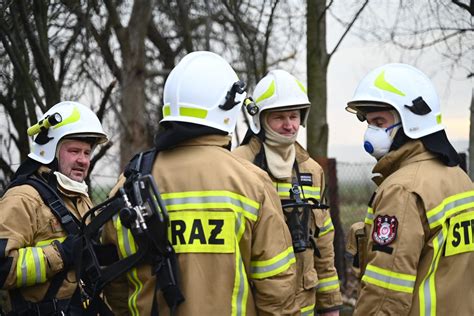 Zdjęcie przedstawiające akcję gaśniczą strażaków na tle płonącej hali