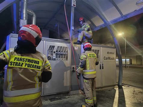 Zdjęcie strażaków pracujących na miejscu pożaru, dym wydobywający się z budynku