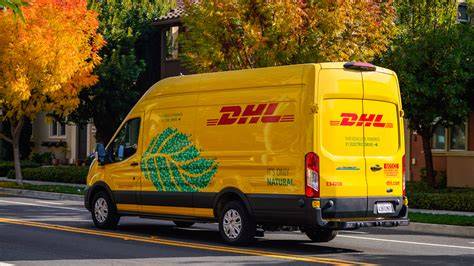 Photo showing burnt DHL delivery vans on a parking lot, with firefighters in the background.
