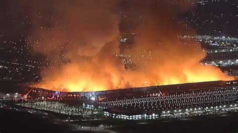 Thematic photo of a large warehouse fire at night with many firefighters and smoke
