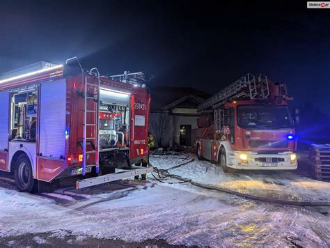 Zdjęcie przedstawiające akcję gaśniczą strażaków przy płonącym domu jednorodzinnym w nocy.