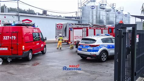 Zdjęcie przedstawiające akcję gaśniczą straży pożarnej przy dużej hali magazynowej w warunkach silnego zadymienia.