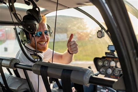 Pilot śmigłowca w kokpicie, wykonujący precyzyjny manewr zawisu nad ziemią