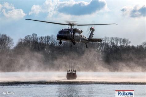 Policyjny śmigłowiec Black Hawk z podwieszanym zbiornikiem Bambi Bucket w akcji gaśniczej nad płonącym lasem