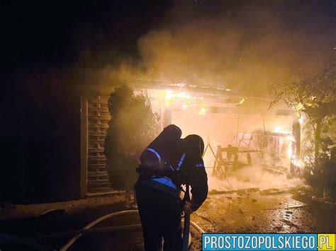 Zdjęcie nocne: strażacy gaszący pożar budynku gospodarczego i samochodów pod wiatą