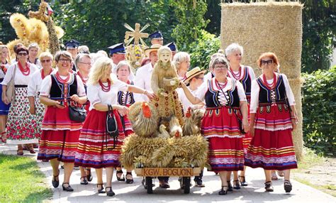 Zgromadzenie ludzi podczas dożynek z elementami tradycyjnych dekoracji i wozów dożynkowych