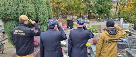 Zdjęcie z ceremonii pogrzebowej, przedstawiające strażaków oddających hołd lub kondukt żałobny