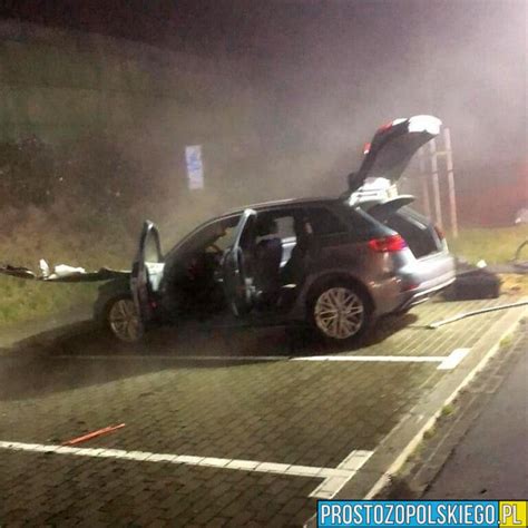 Zdjęcie spalonego samochodu na parkingu oraz strażaków