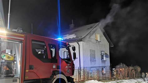 Zdjęcie płonącego balkonu w budynku mieszkalnym, z widocznymi pękającymi oknami i interwencją policjanta.
